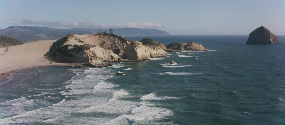 Weak waves crash into the beach shoreline as mountains loom behind