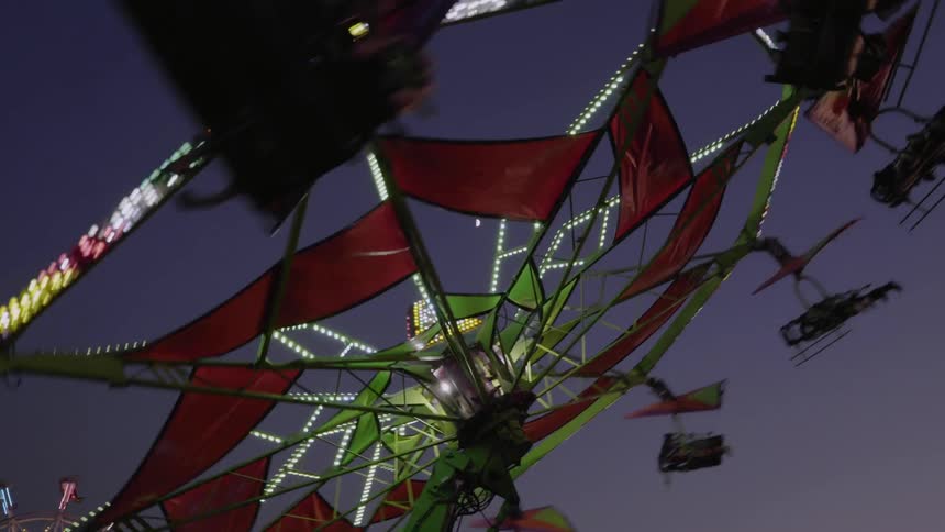 Park ride covered by red banners rotates in the night