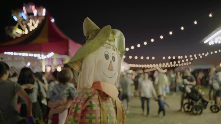 A large scarecrow stands in the middle of an autumn carnival