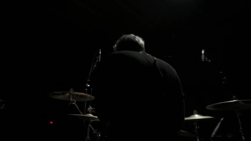 A man plays the drums on a dark stage