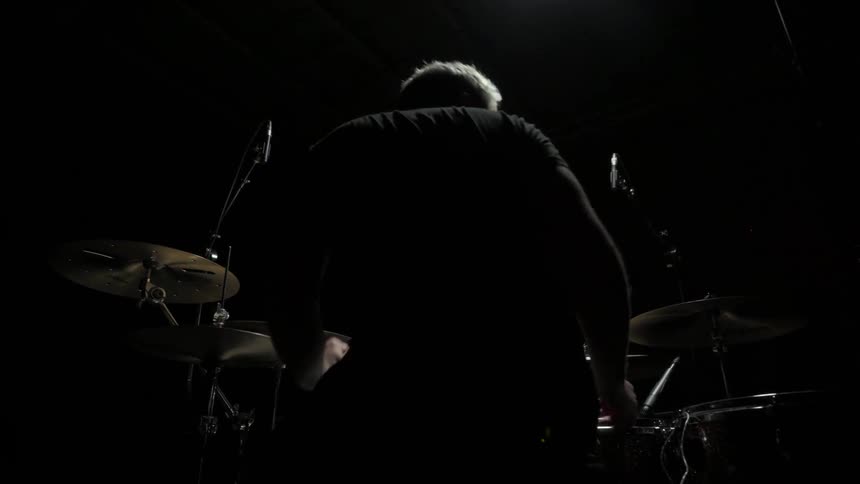 Man gets ready to play drums in the spotlight on the dark stage