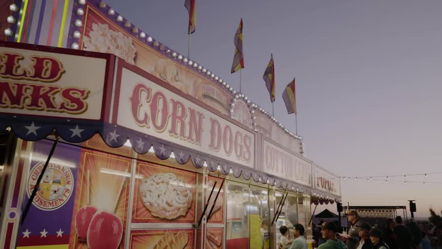 People wait in line for a concession stand with corn dogs cotton candy and cold drinks at a carnival