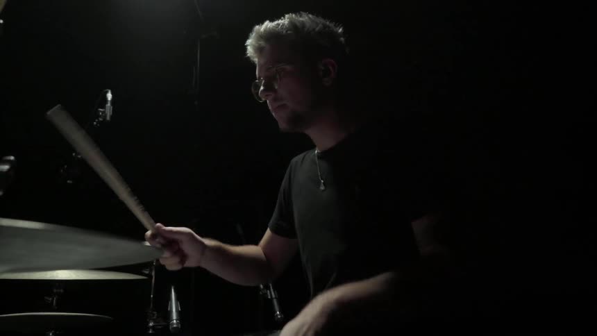 A young white man plays a drum kit