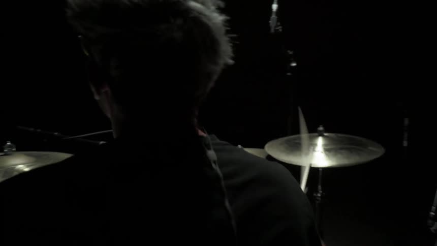 Man plays drum in the spotlight in a dark room