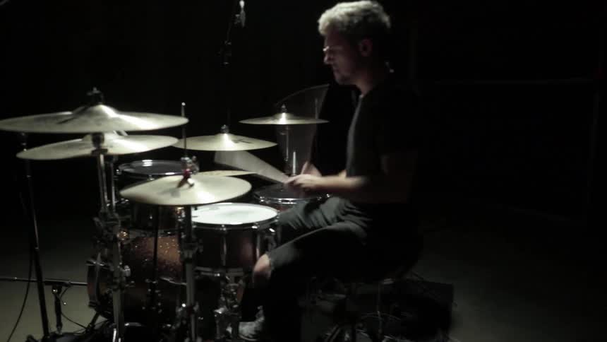 A man plays the drums in a dark room