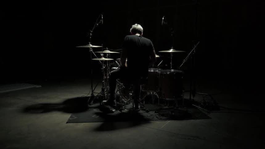 A man walking up to a drum set and sitting down