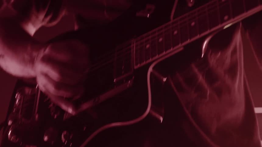 A man plays an electric guitar under stage lighting