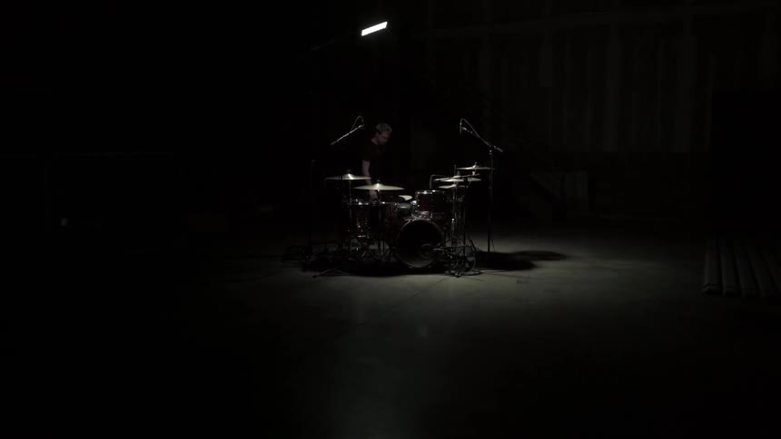 Drummer comes from the dark and sits behind his drum kit