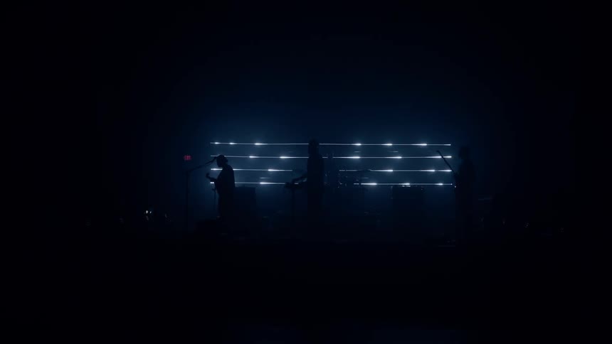 A very dark stage is barely lit by horizontal arrays of led lights as the silhouettes of the band members can be seen as they perform their instruments