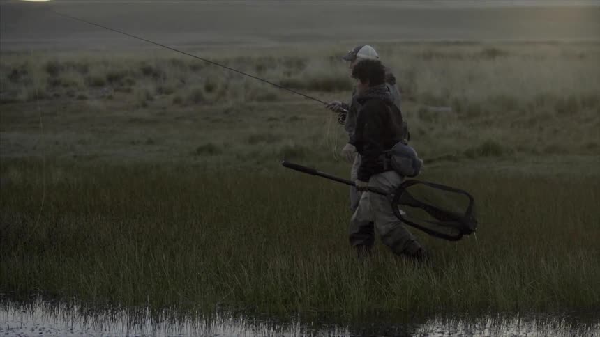 Two men walking in a marsh one is carrying a fishing rod and the other a large net