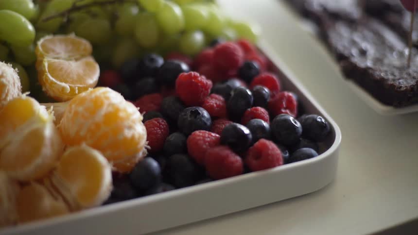 Assorted fruit is in a tray on a table along with brownies