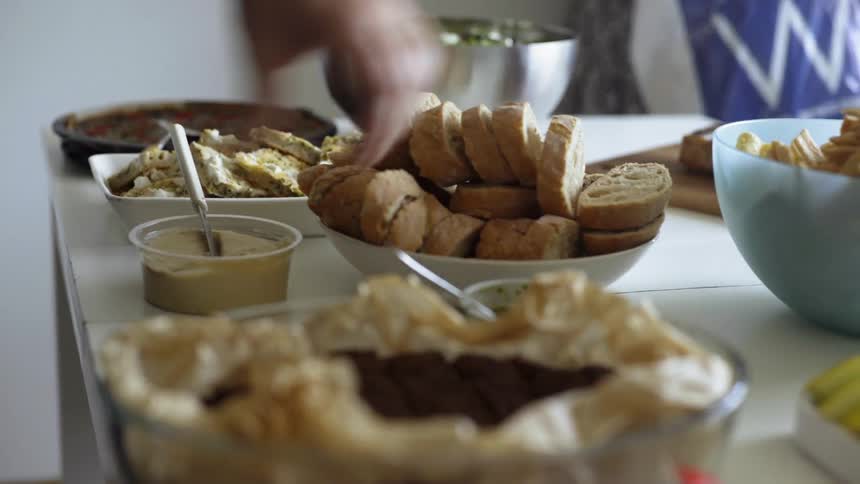 A white woman moves a couple of dipping sauces on a table loaded with food