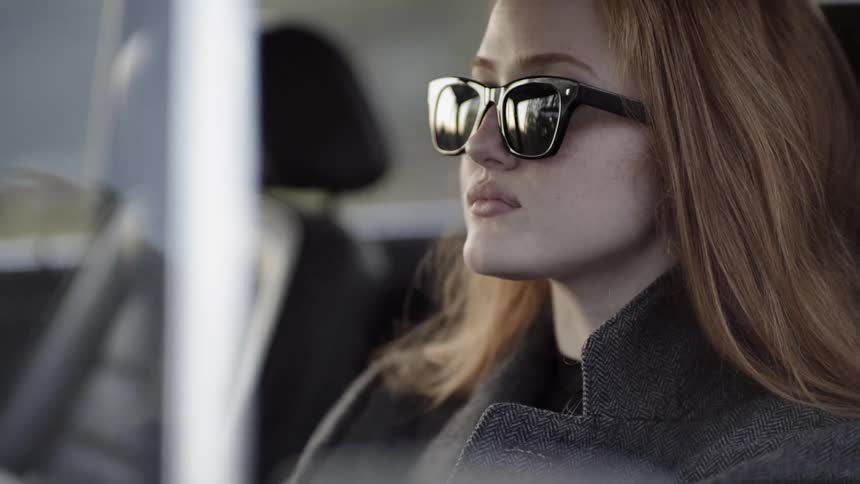 A woman is sitting in the car wearing sunglasses