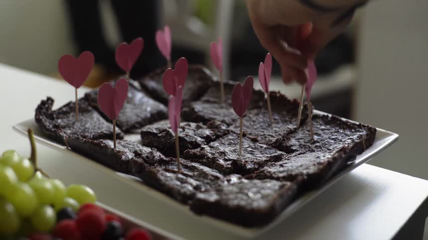 A person places heart shaped decorations in brownies