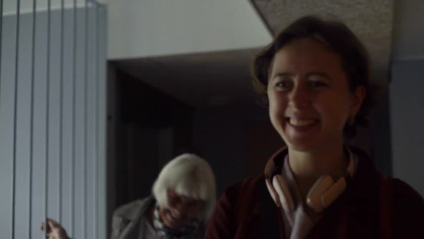 A woman with a big smile on her face opens a door slowly and walks up to a person in the room and gives them a loving hug