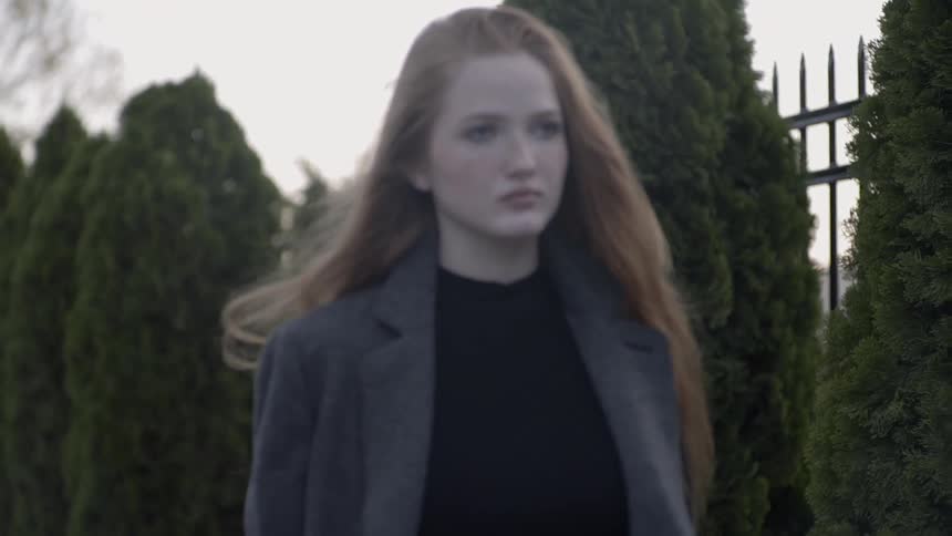 Ginger hair woman looks ahead and walks outdoors during daylight