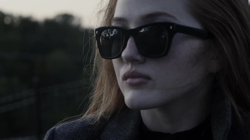 A young white woman wearing sunglasses runs her hand through her hair