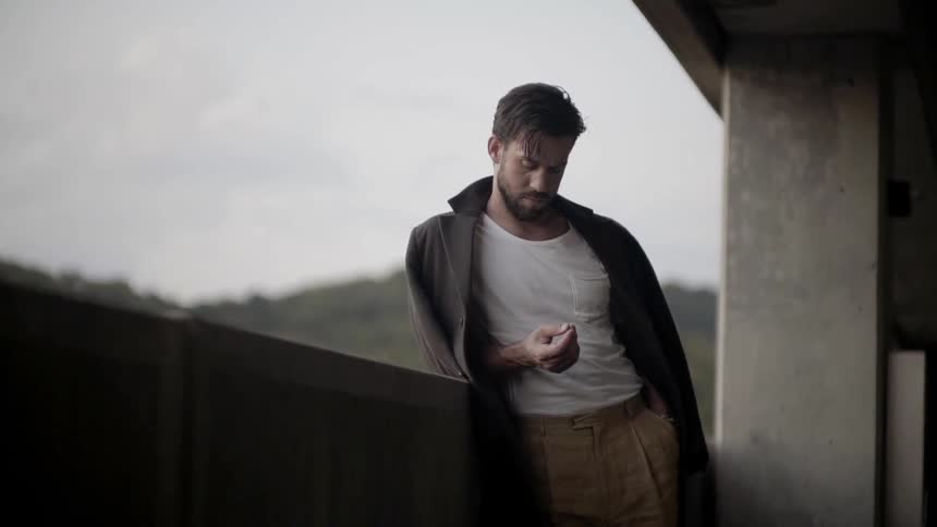 A white man leans against a concrete barrier and looks around his surroundings