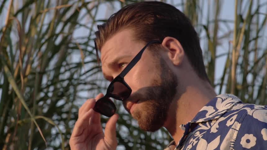 Man takes off sunglasses and looks ahead at sunset