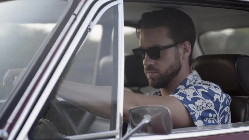 A white man wearing sunglasses drives a car