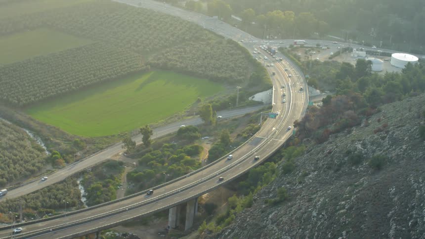 The cars drive around the overpass past the hill