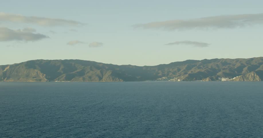 A range of mountains are seen lining a coastal area at the edge of a calm ocean