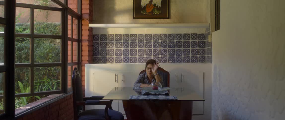 Old woman wearing glasses sits at table and closes eyes indoors during daylight
