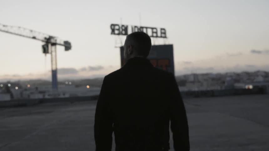 Man walks on a concrete roof of a large building towards a billboard