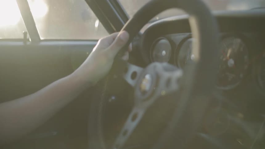 Woman with tattoo on her wrist holds steering wheel and changes gears while driving at sunset