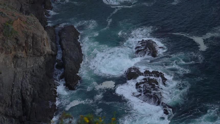 At the edge of a jagged cliff which plunges into the ocean there are several treacherous rocks that protrude out of the surface of the water causing the waves to violently swirl around them