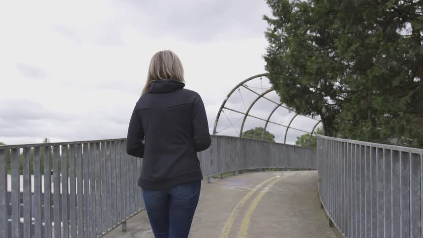 A woman walking on a fence lined path past a tree