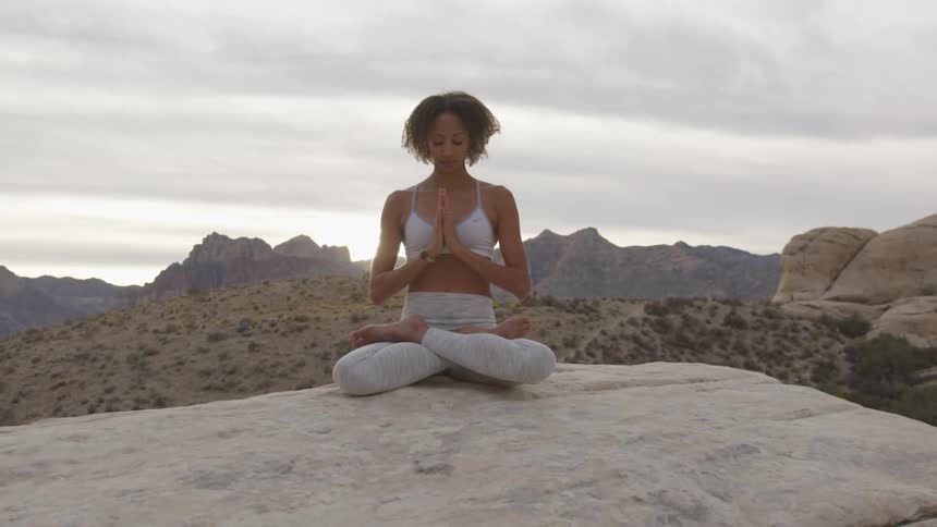 A woman sitting on a rock meditating