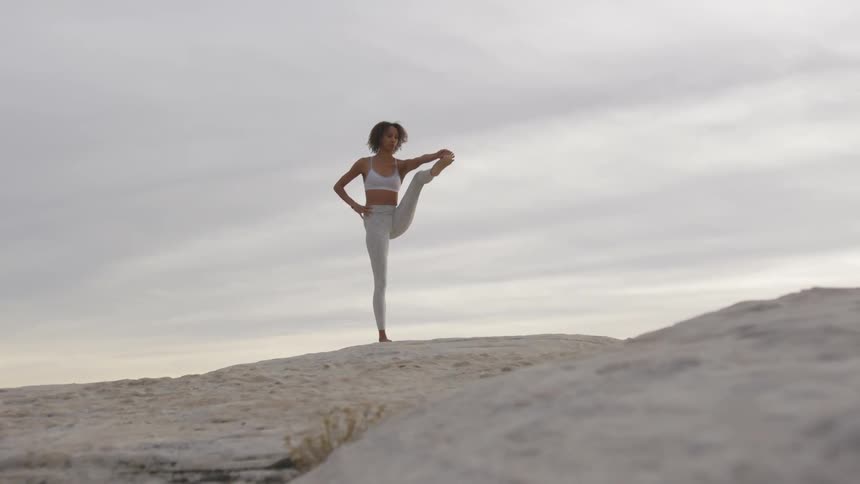 A black woman stretches out one leg while standing on a rock