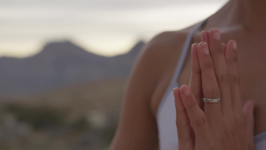 A woman wearing a ring is standing with her palms together