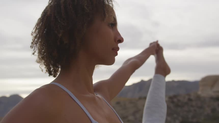 A woman extends her leg doing a yoga pose in mountains