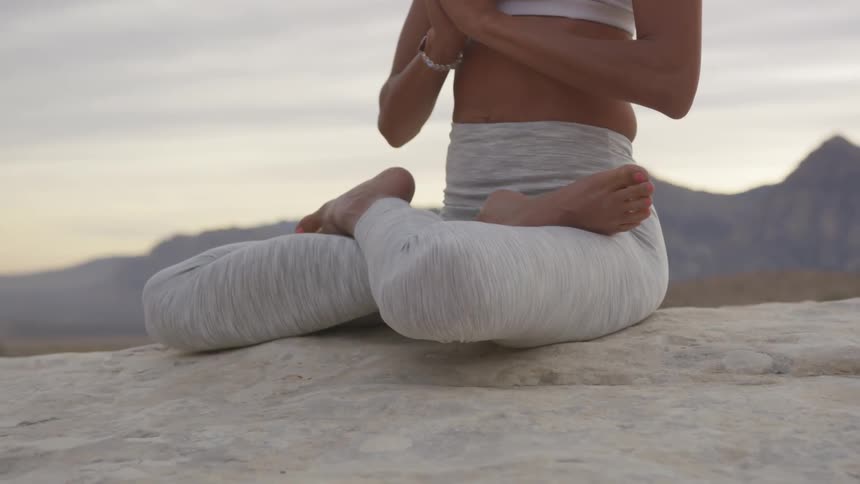 A black woman practices yoga while sitting on a rock in a desert