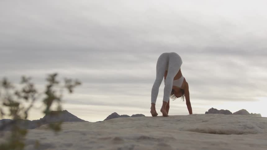 A woman outside stretching with mountains and the sky in the background