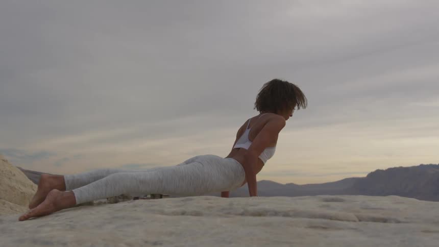 A woman is doing a push up and a back stretch on a rocky hill