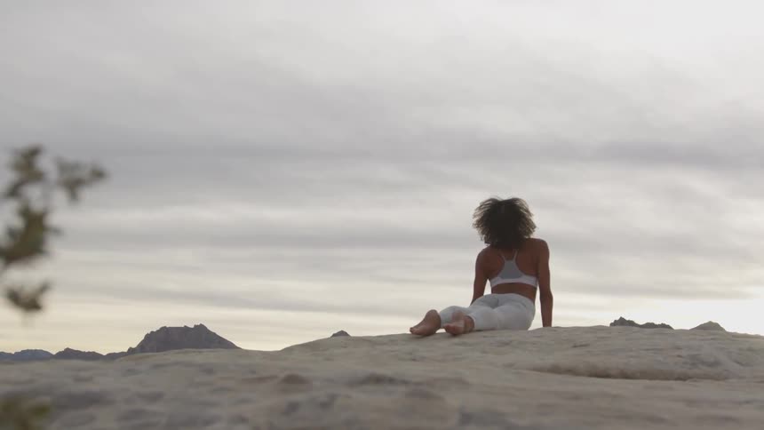 Woman practicing yoga on a desert at sunset