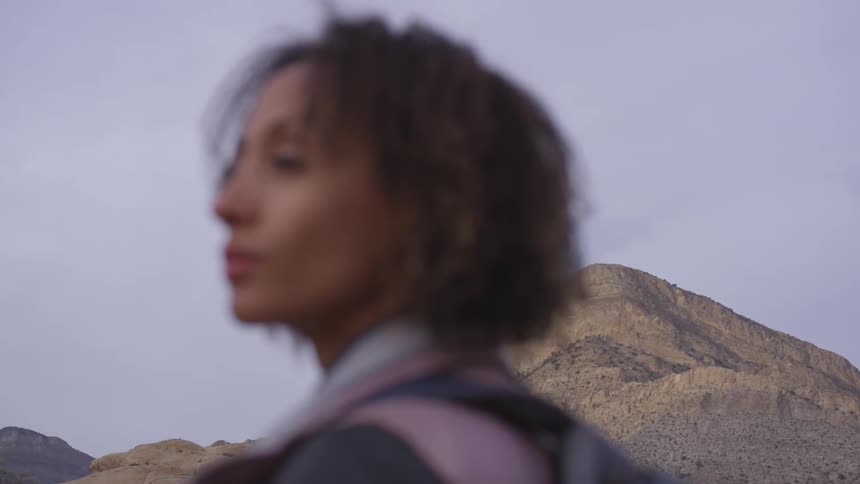 Woman stands outdoors with rocky hill in the background