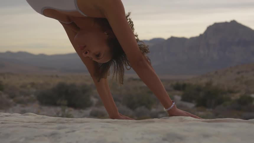 Brunette woman stretches her body on a big rock outdoors on a cloudy day