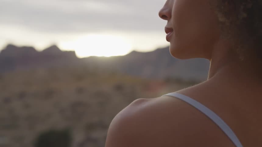 A young thin woman stands outside looking out over a desert landscape