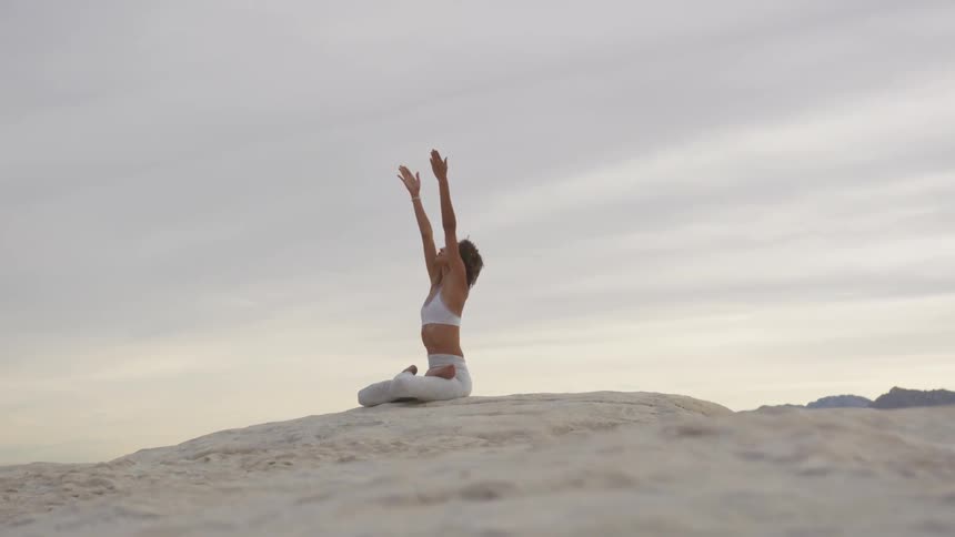 Woman doing yoga on a desert at sunset
