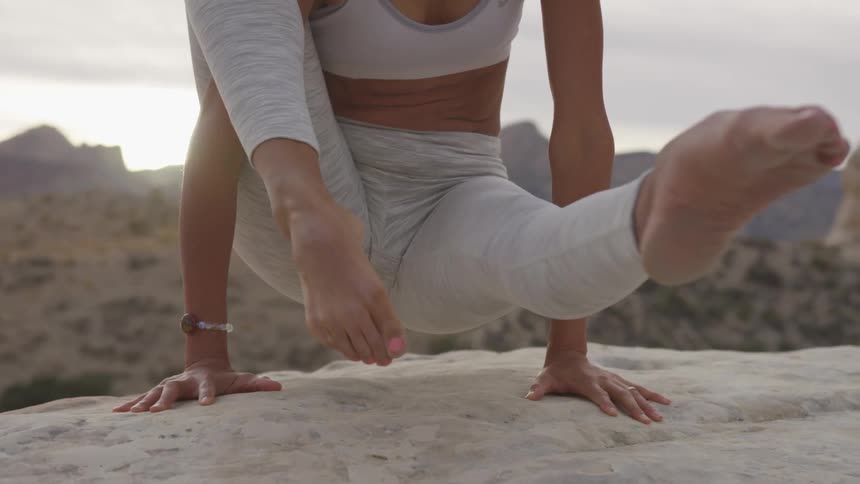 A young woman holds a yoga pose on a mountain