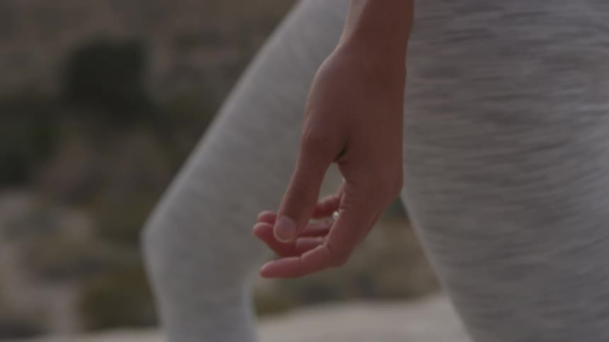 A woman in tight exercise pants stands still as she holds a yoga pose and her hand hangs freely in a relaxed position
