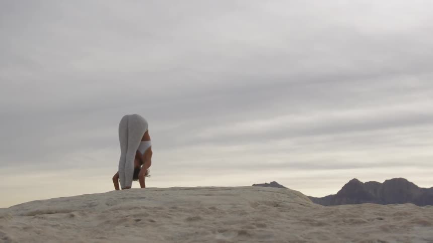 A black woman stands on a rock in a desert and bends at the waist