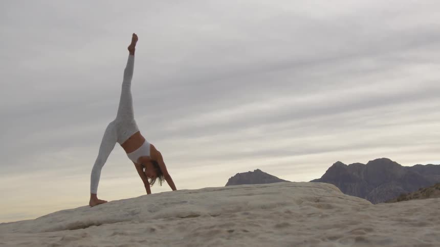 Woman practicing yoga on a desert at sunset