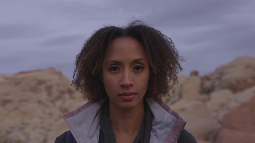 A woman is standing in front of a rocky hill