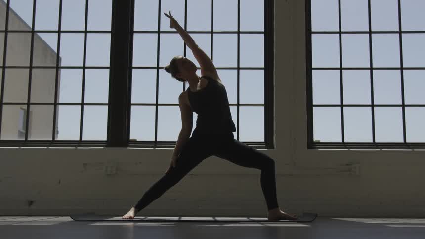 A woman does yoga in front of windows in a yoga studio