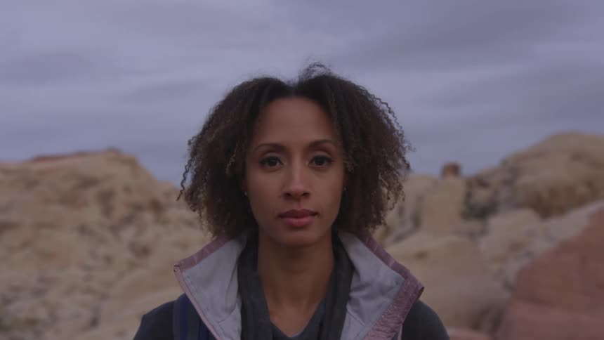 A woman looks into the camera while standing in the desert